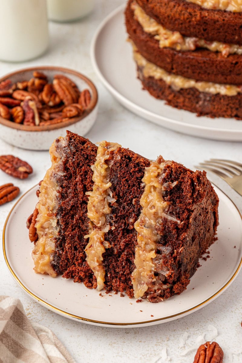 a slice of German chocolate cake on a white plate with remaining cake in the background