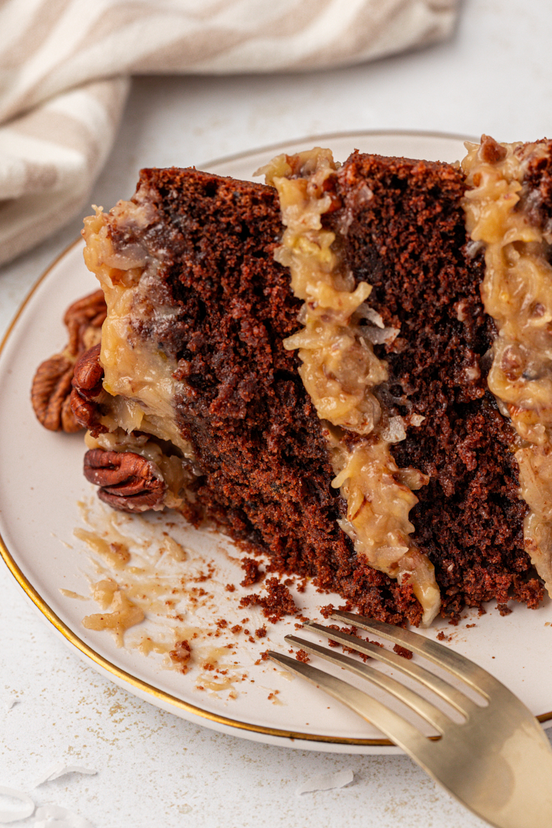 a slice of German chocolate cake on a plate with a bite missing and a fork resting on the edge