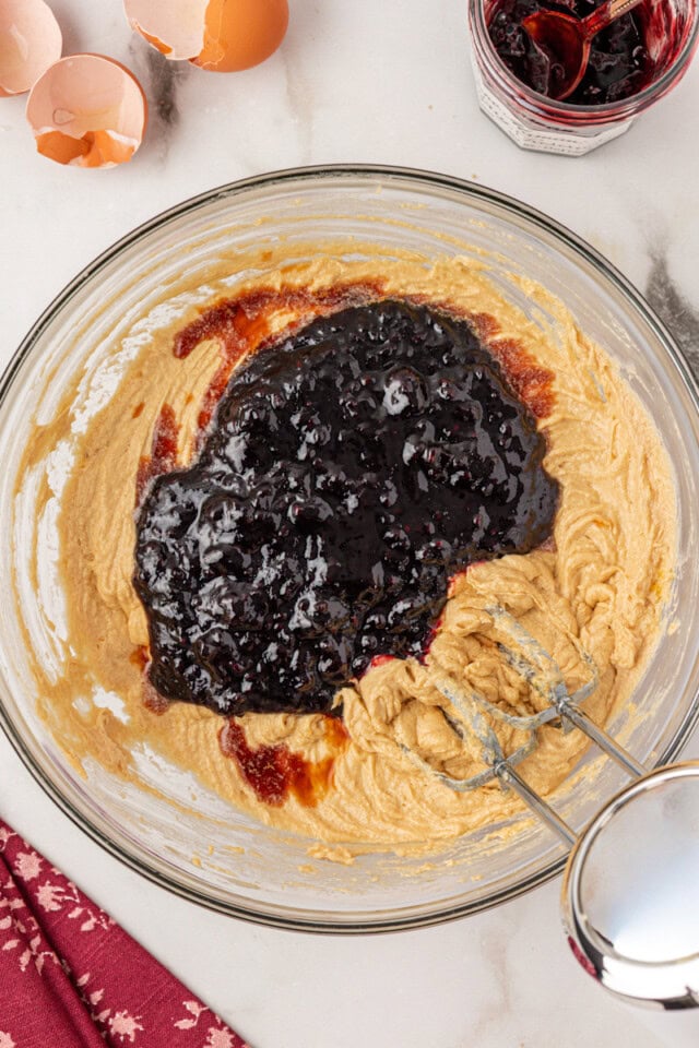 overhead view of blackberry jam and vanilla extract added to partially mixed cake batter