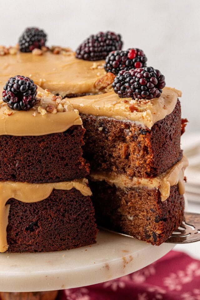 A sliced Kentucky Jam Cake showing its moist, spiced interior, with caramel frosting between the layers and on top, garnished with blackberries and chopped pecans.