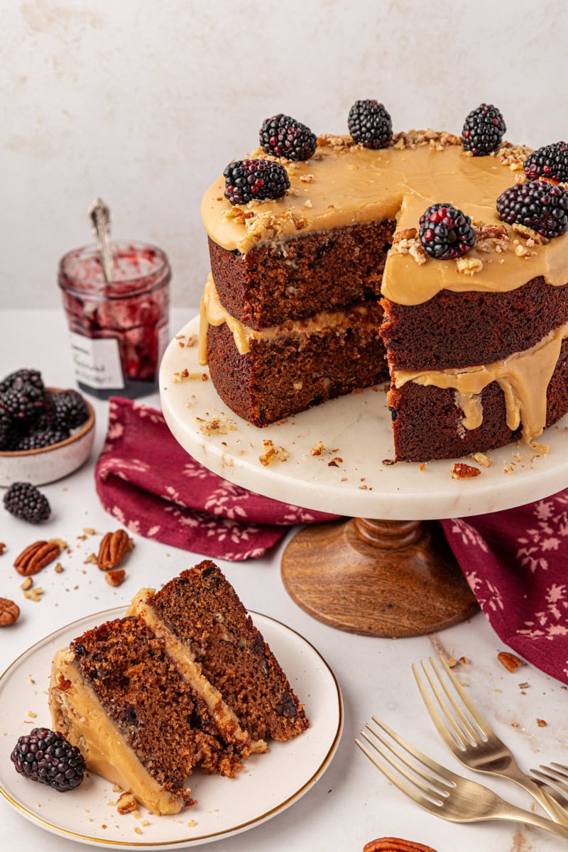 a slice of Kentucky jam cake on a white plate beside the remaining cake on a marble cake stand