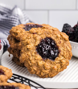 an oatmeal thumbprint cookie leaning against a short stack of more cookies on a white plate