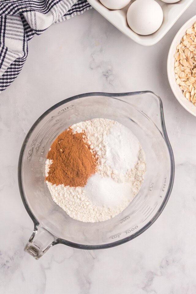 overhead view of flour, baking soda, cinnamon, and salt in a glass mixing bowl