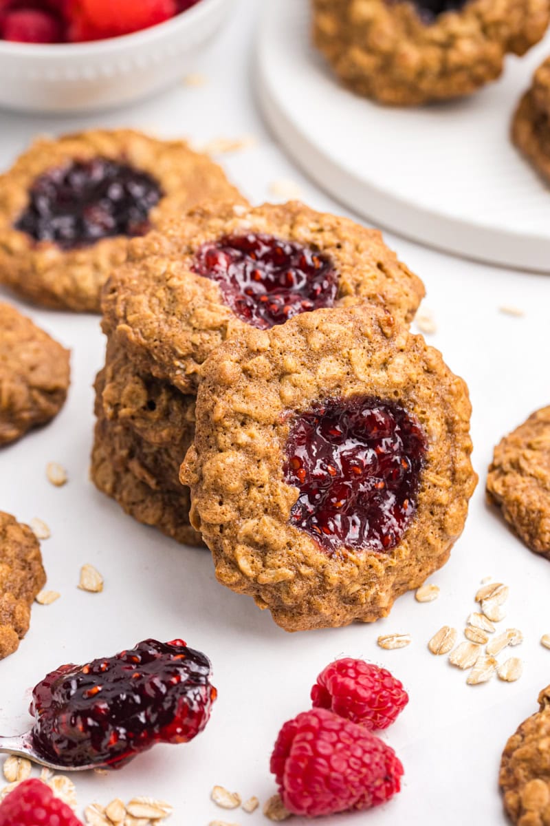 a stack of oatmeal thumbprint cookies with another cookie leaning against the stack; more cookies, raspberries, and blackberries surrounding