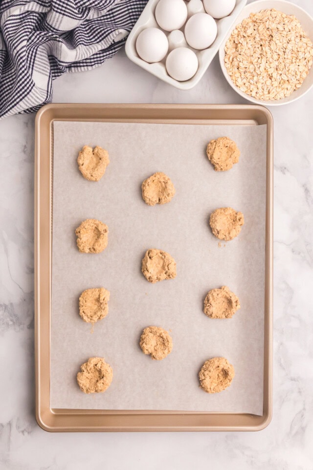 overhead view of oatmeal thumbprint cookies shaped on a lined baking sheet