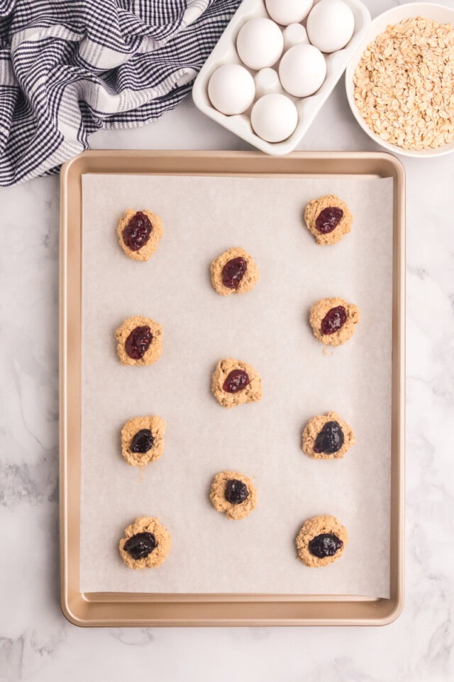overhead view of oatmeal thumbprint cookies on a parchment-lined baking sheet ready to go into the oven