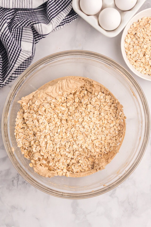 overhead view of oats added to cookie dough in a glass mixing bowl