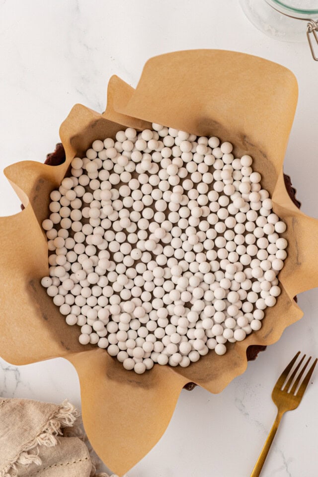overhead view of unbaked chocolate tart dough lined with parchment paper and filled with pie weights, ready to go into the oven