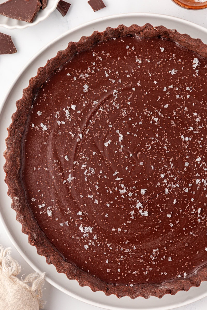overhead view of salted dark chocolate tart topped with flaky se salt and served on a white serving plate