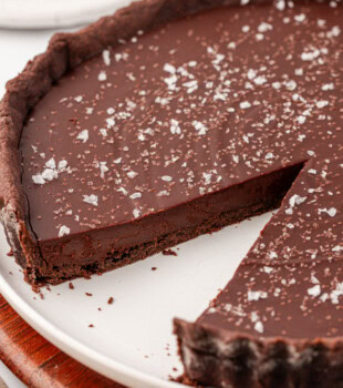 salted dark chocolate tart on a white serving plate with a slice missing