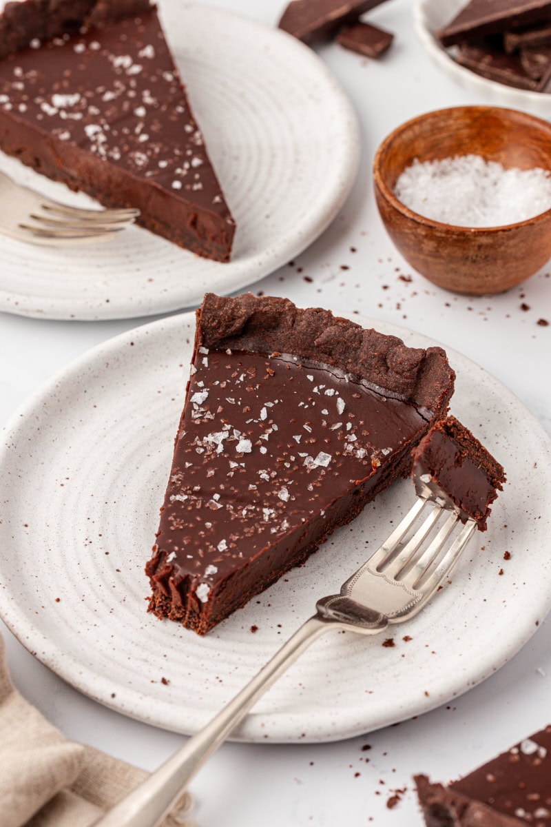 a slice of salted dark chocolate tart on a white plate with a bite on a fork