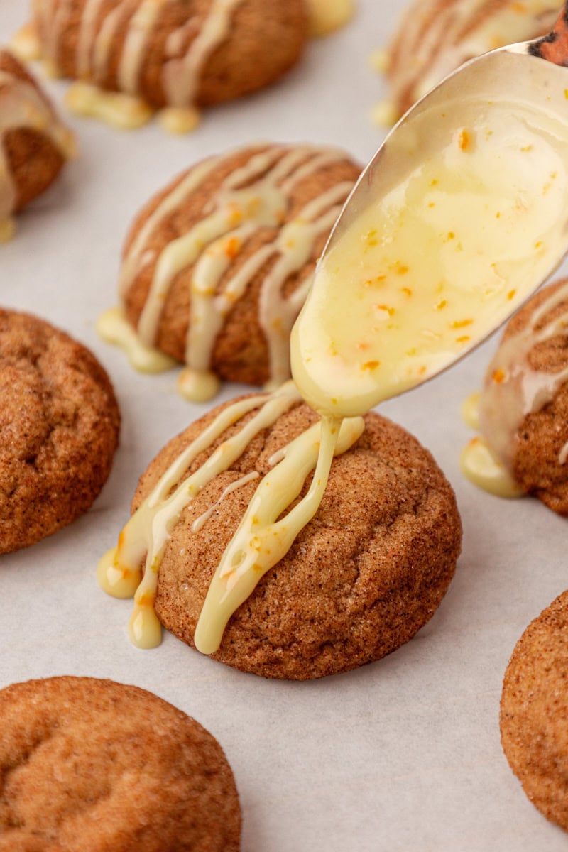 orange glaze in a spoon drizzling over a sugar and spice cookie