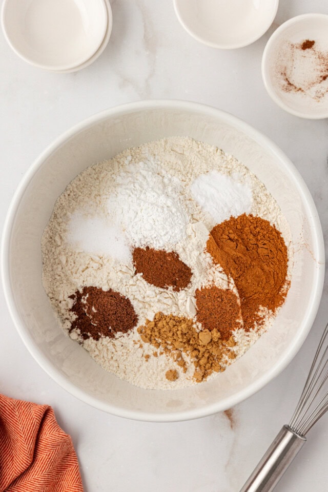 overhead view of flour, baking powder, baking soda, salt, and spices in a white mixing bowl