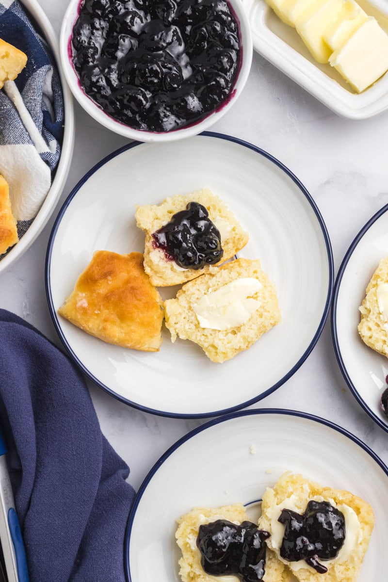 overhead view of touch of grace biscuits topped with blueberry jam on blue-rimmed white plates