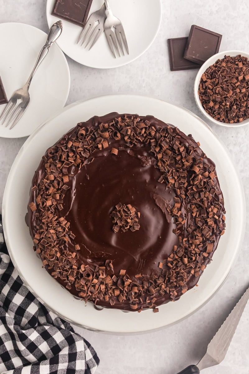 overhead view of brownie bottom chocolate cheesecake topped with chocolate curls on a white cake stand