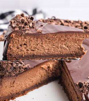 a slice of brownie bottom chocolate cheesecake on a pie server with the remaining cheesecake in the background