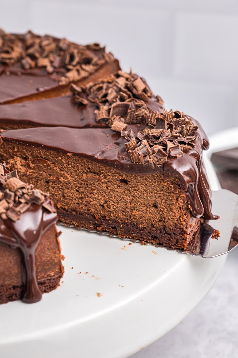 partially sliced brownie bottom chocolate cheesecake on a white cake stand