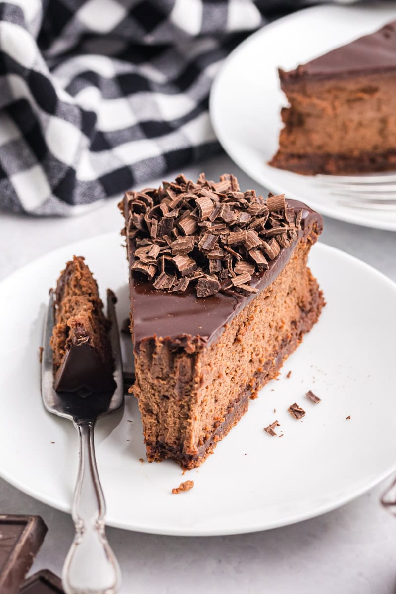a slice of brownie bottom chocolate cheesecake on a white plate with a bite on a fork