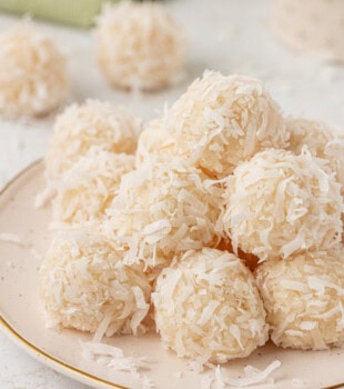 coconut snowballs served on a white plate with more of the candies in the background