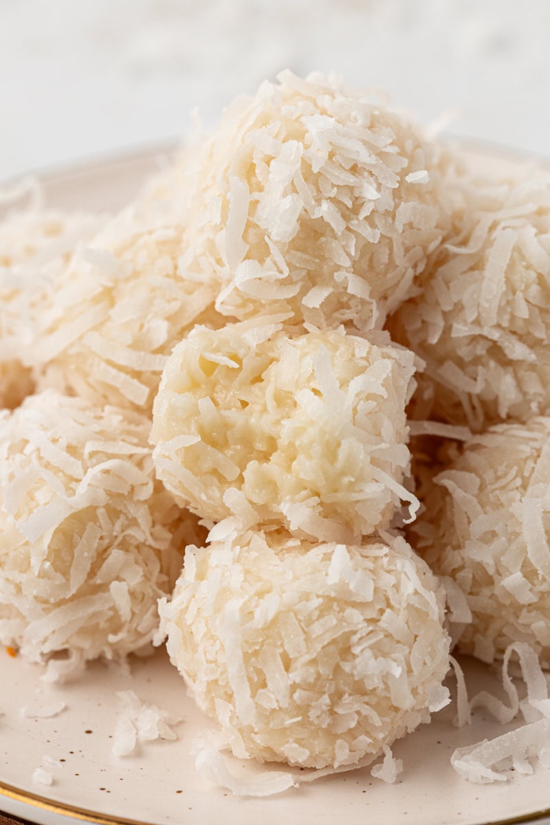 a pile of coconut snowballs on a white plate with a bite missing from one of them