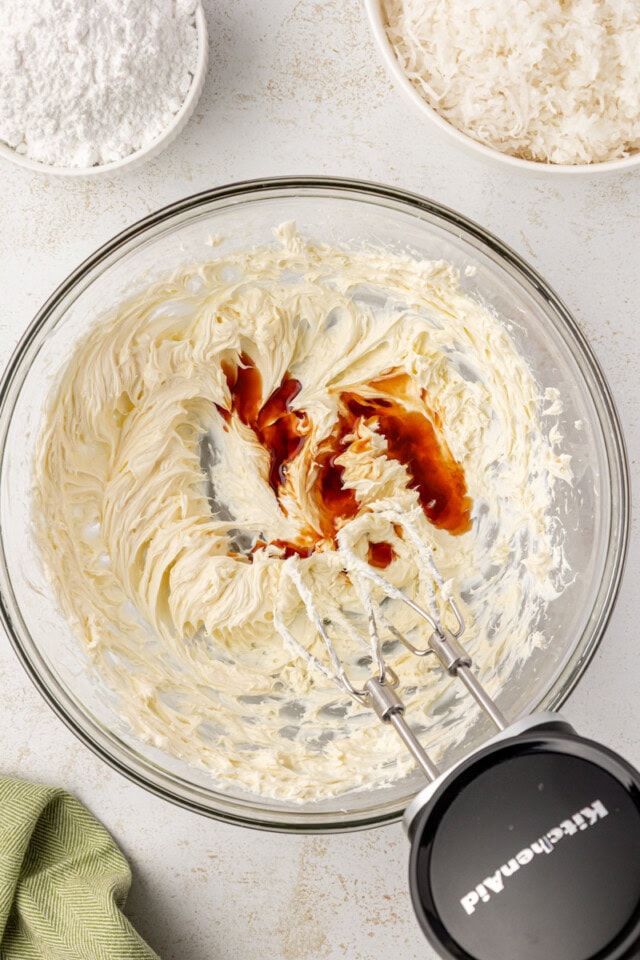 overhead view of vanilla and almond extracts added to beaten cream cheese