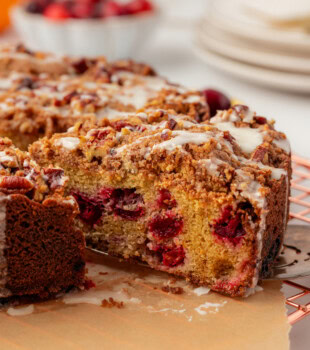 a slice of cranberry coffee cake on a cake server being pulled away from the remaining cake