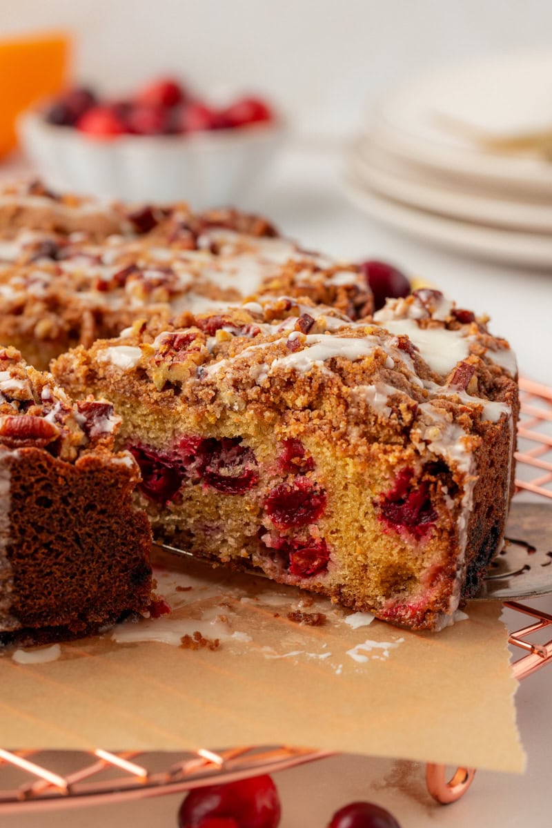 a slice of cranberry coffee cake on a cake server being pulled away from the remaining cake
