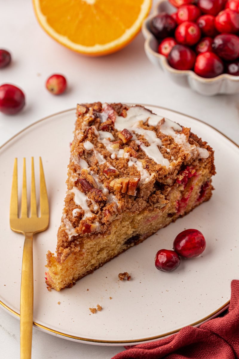 a slice of cranberry coffee cake topped with an orange glaze served on a white plate