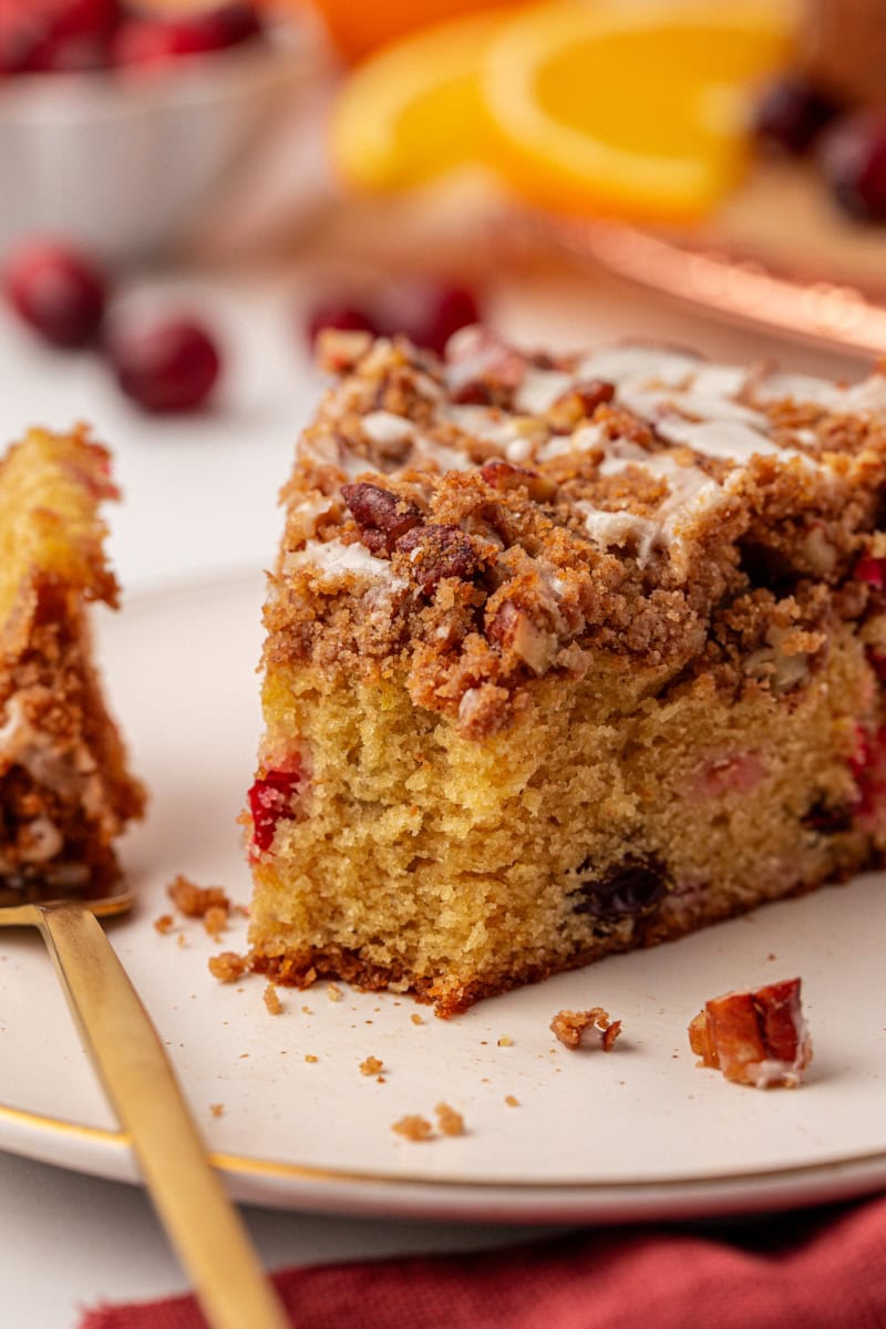 a slice of cranberry coffee cake on a plate with a bite on a fork resting alongside