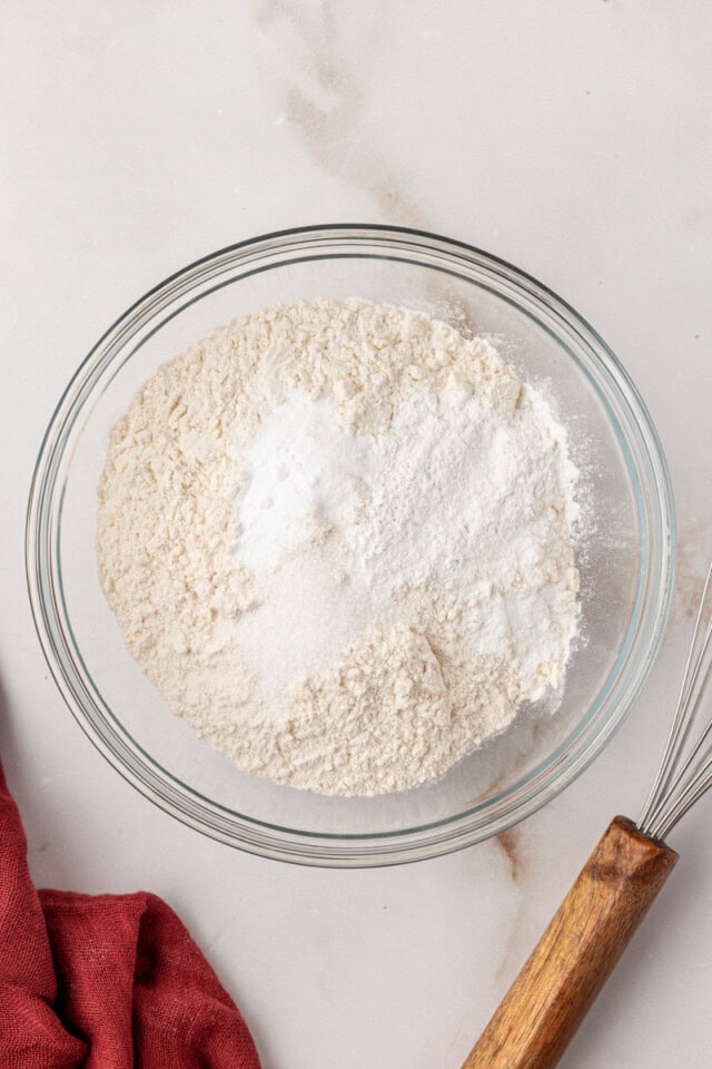 overhead view of flour, baking powder, baking soda, and salt in a glass mixing bowl
