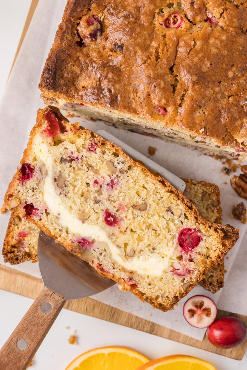 a slice of cranberry cream cheese bread on a serving spatula with the remaining bread in the background