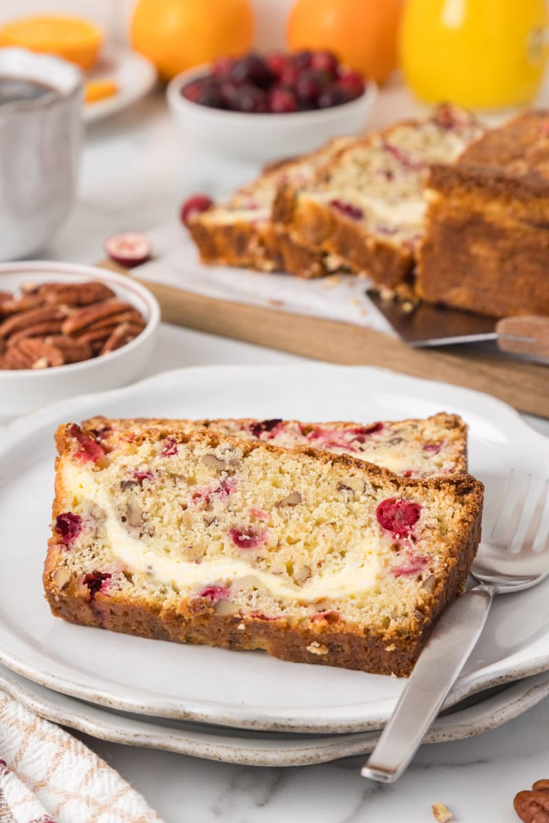 two slices of cranberry cream cheese bread on a white plate with more bread in the background