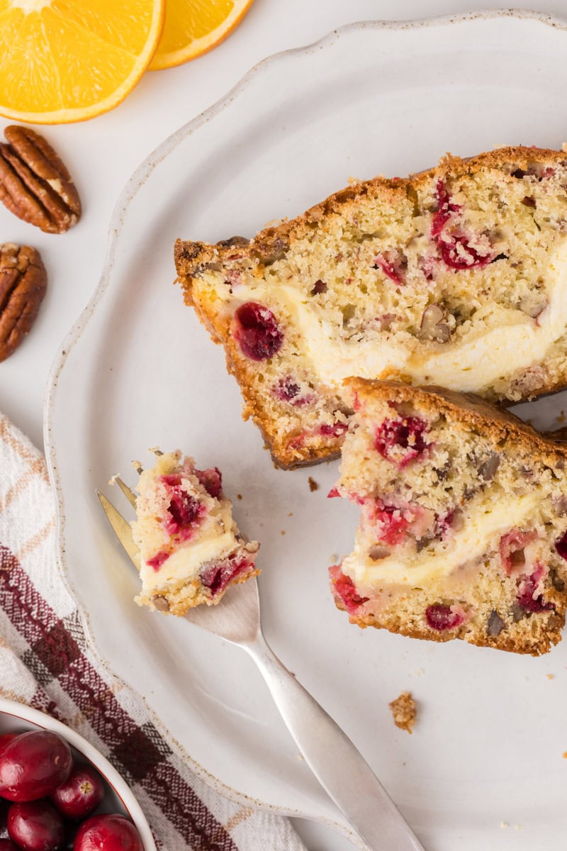 overhead view of two slices of cranberry cream cheese bread on a white plate with a bite on a fork