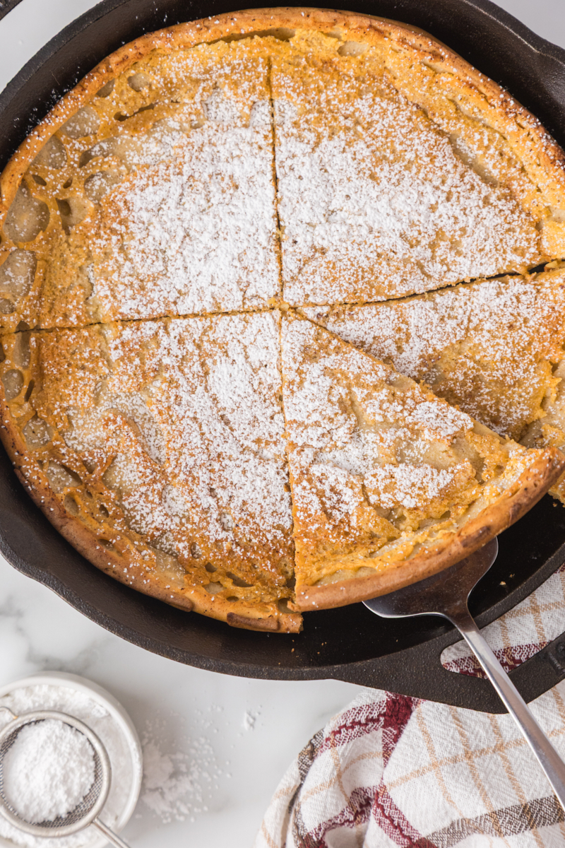 overhead view of a slice of Dutch baby pancake being lifted from the remaining pancake in a cast iron skillet