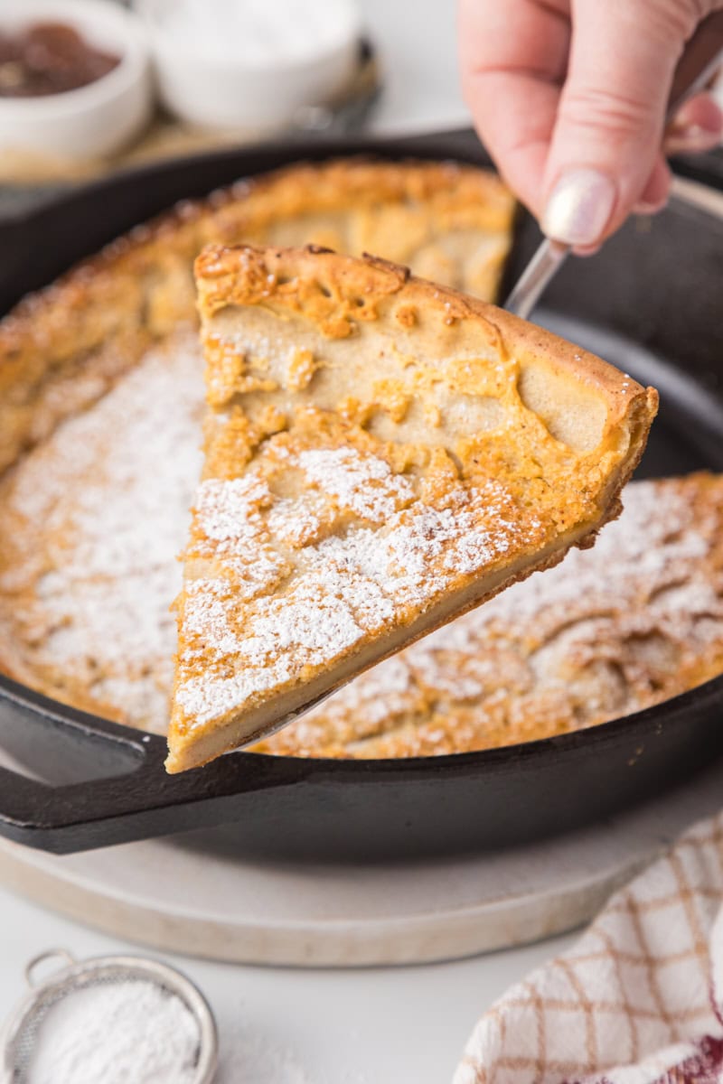 a slice of Dutch baby pancake on a pie server with the remaining pancake in the background