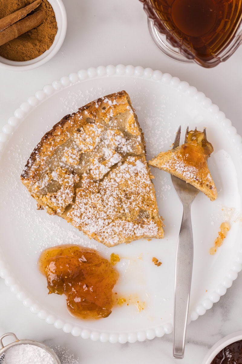 a slice of Dutch baby pancake on a white plate with a bite on a fork and a dollop of jam