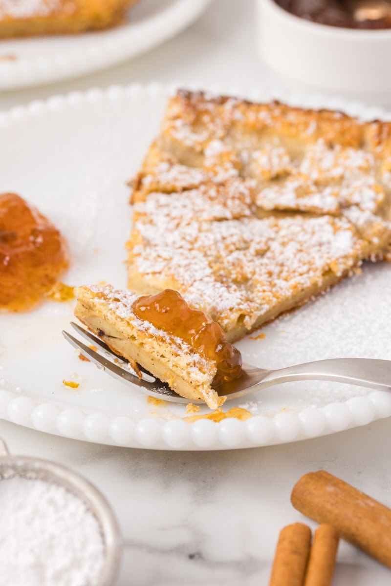 a bite of Dutch baby pancake topped with jam on a fork with the remaining serving behind