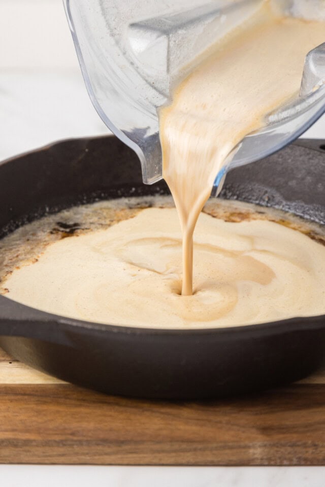 Dutch baby pancake batter being poured into melted butter in a cast iron skillet