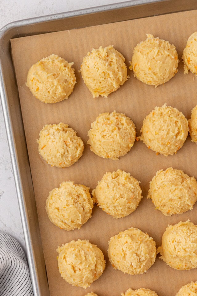 overhead view of scooped orange cookie dough on a parchment-lined baking sheet