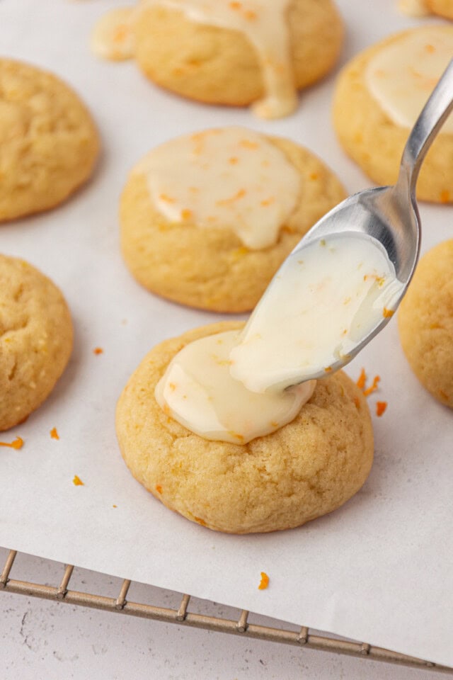 orange icing being spooned onto an orange cookie