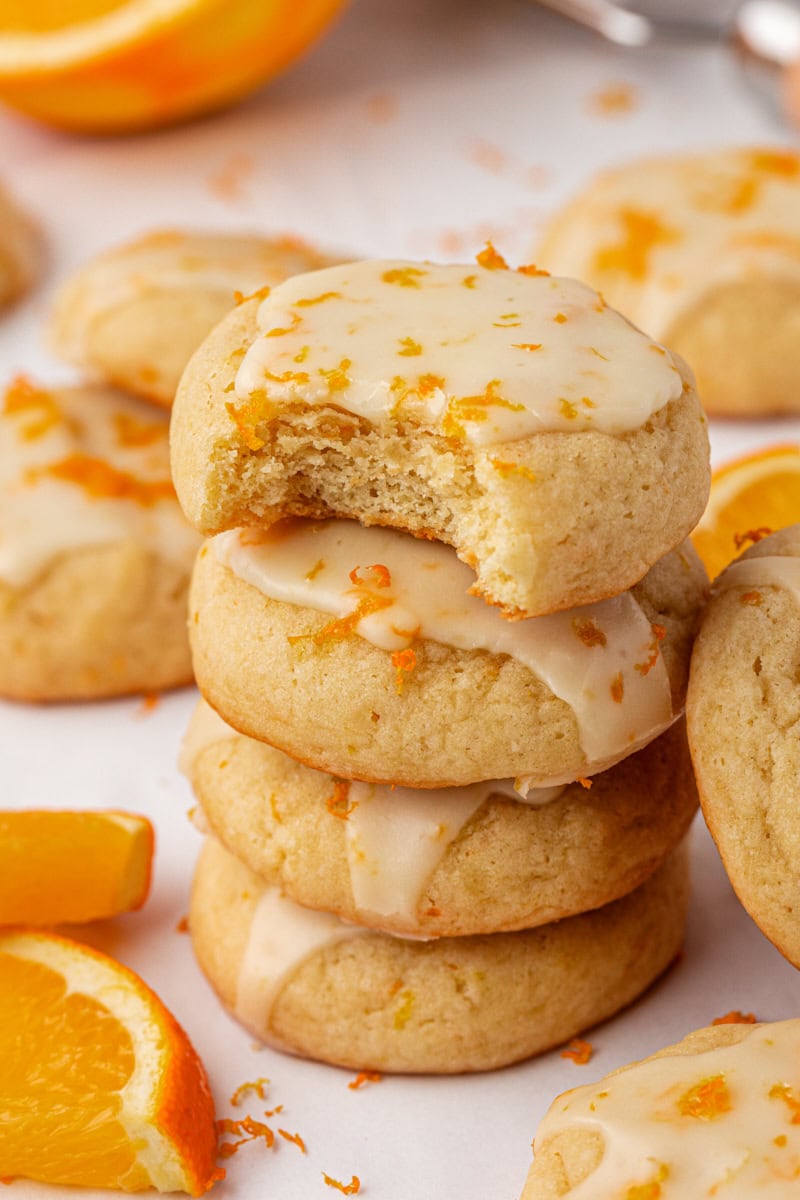 a stack of four glazed orange cookies with a bite missing from the top cookie