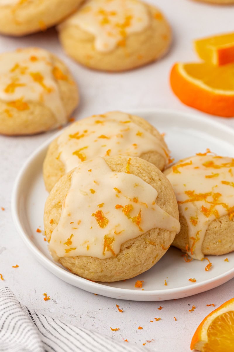 three glazed orange cookies on a white plate with more cookies in the background