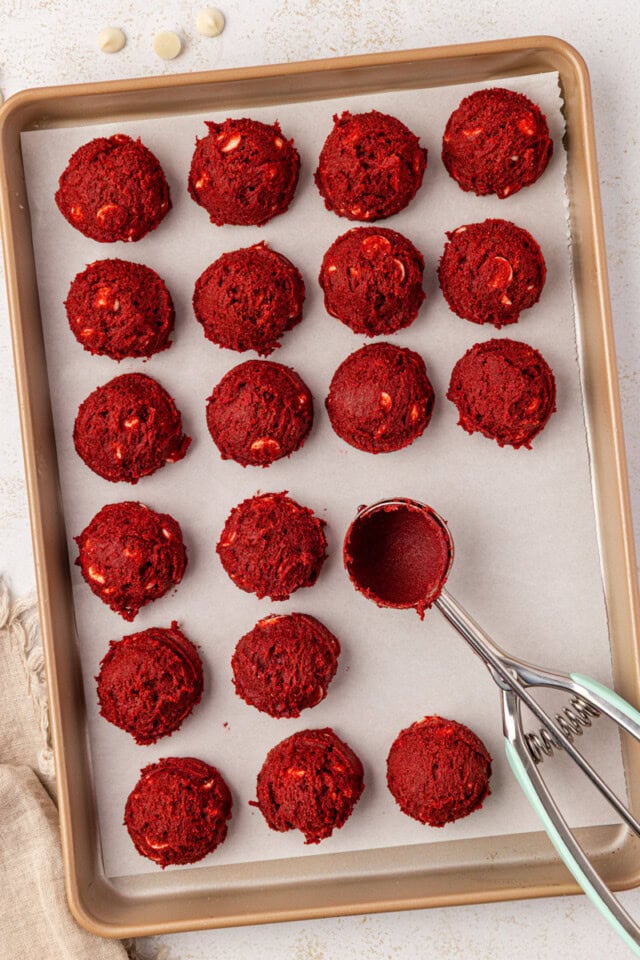 overhead view of scooped red velvet cookie dough on a parchment-lined baking sheet ready for chilling