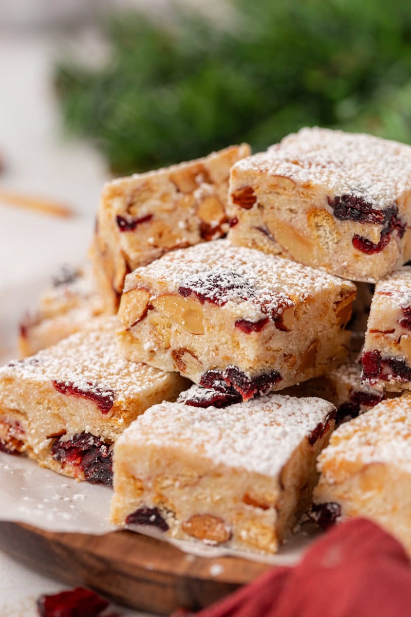 snowflake crisp bars made with white chocolate, crackers, dried cranberries, and nuts, dusted with powdered sugar and stacked on parchment paper