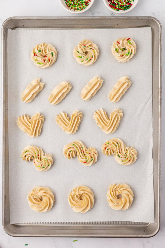 overhead view of whipped shortbread cookies piped into various shapes on a parchment-lined baking sheet