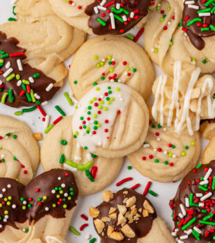 whipped shortbread cookies in various shapes topped with garnishes such as sprinkles, chocolate, and nuts