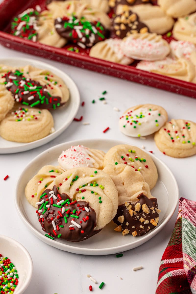 several whipped shortbread cookies on a white plate with more cookies in the background