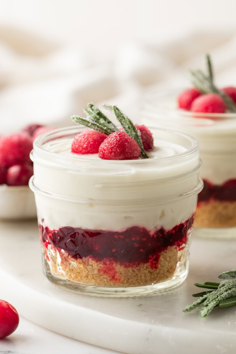 a no-bake white chocolate cranberry cheesecake jar on a marble surface with more jars in the background