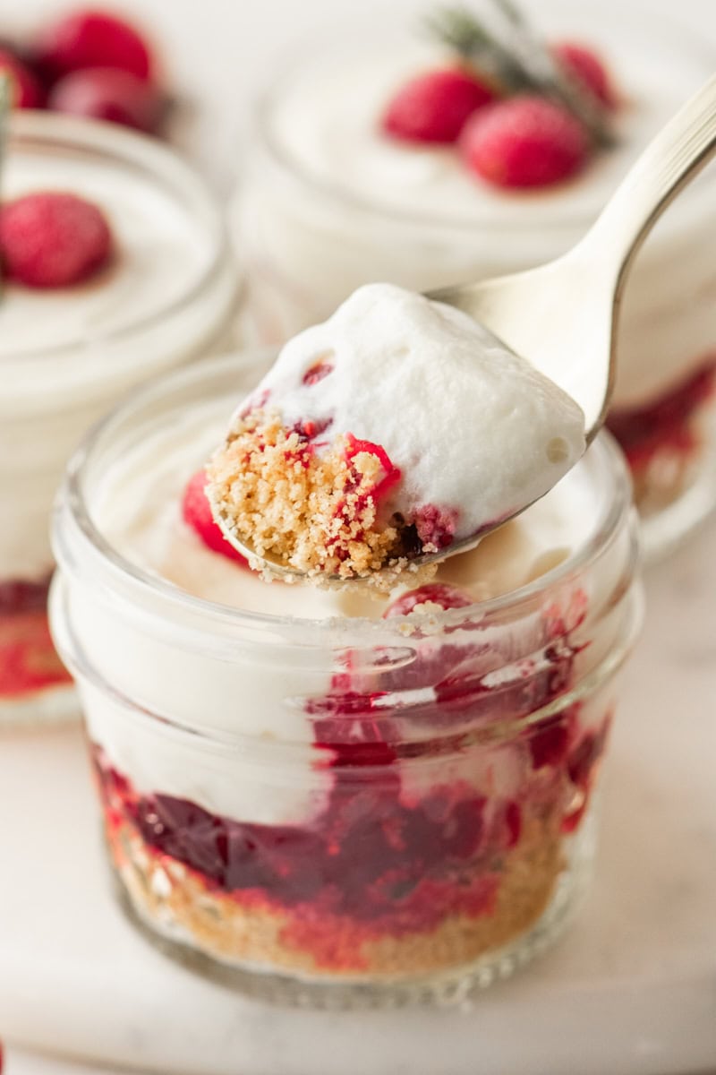 a spoonful of no-bake white chocolate cranberry cheesecake on a spoon with cranberry cheesecake jars in the background