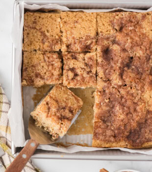 overhead view of partially sliced cinnamon sugar snack cake in a baking pan with a slice on a cake server